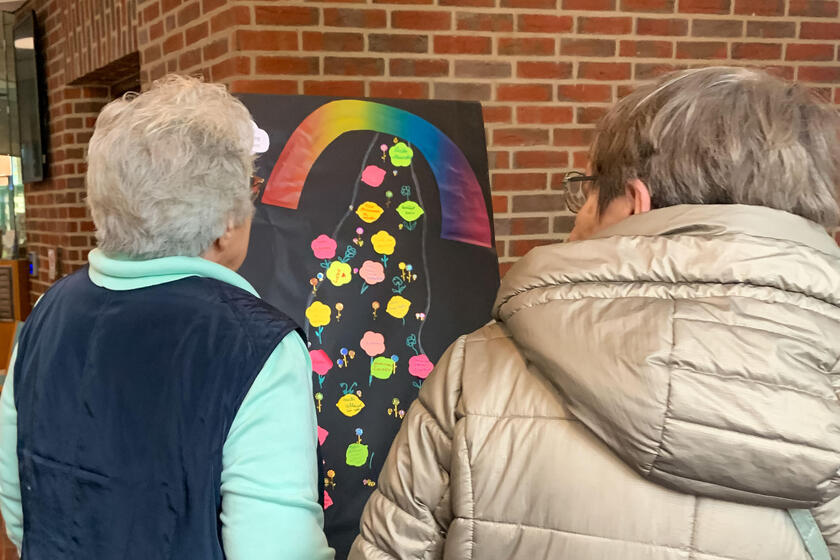 Zwei ältere Frauen stehen vor der Tafel, auf der viele Post-Its geklebt sind.