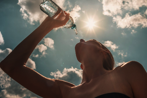 Eine Frau trinkt aus einer Wasserflache. Sie ist von unten gegen den Himmel fotografiert.