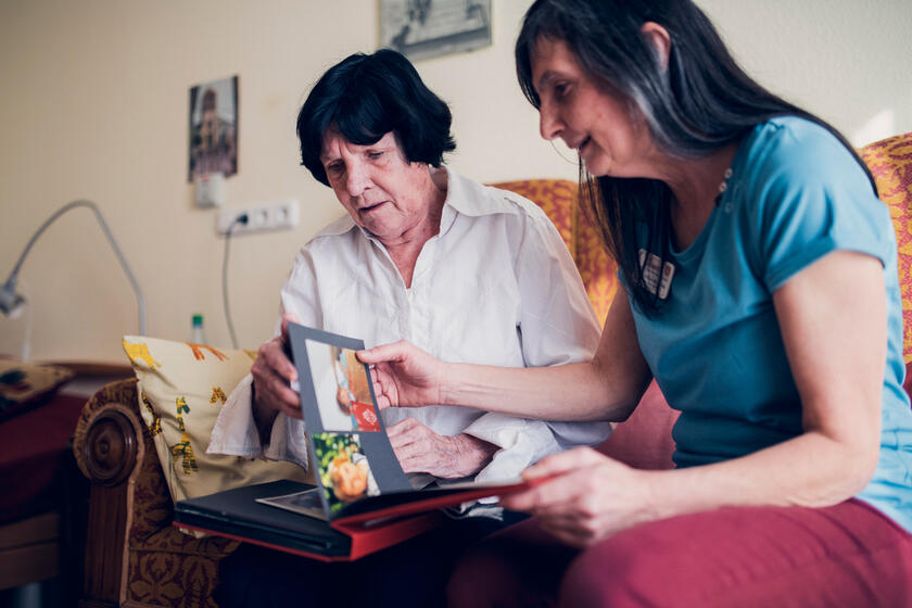 Eine Bewohnerin und eine Mitarbeiterin sitzen in einem Bewohnerzimmer auf einem Sofa und betrachten ein Fotoalbum.