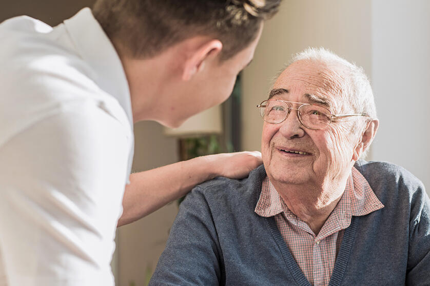 Ein Pfleger legt einem älteren Mann die Hand auf die Schulter.