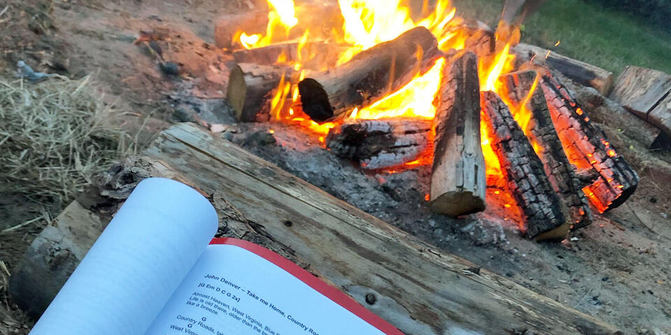 Ein Liederheft, im Hintergrund ist ein Lagerfeuer zu sehen.
