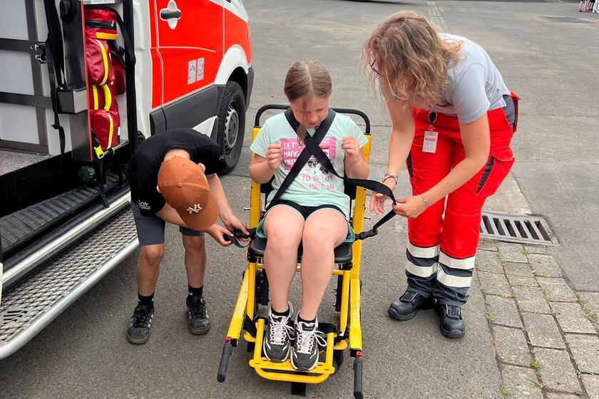 Schulkinder mit Notärztin, die einen Tragestuhl erklärt