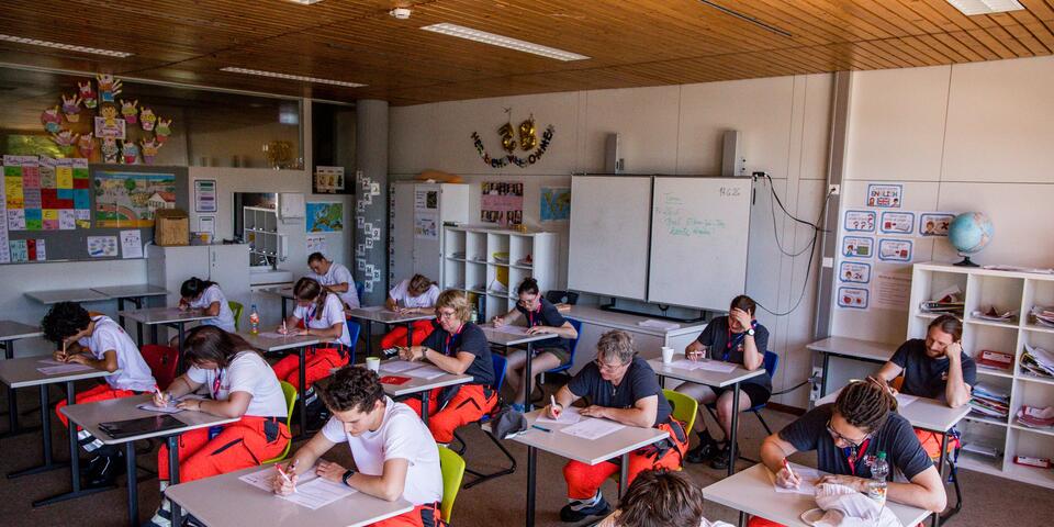 Teilnehmende in Einsatzkleidung sitzen in einem Klassenzimmer und bearbeiten schriftliche Prüfungsbögen.