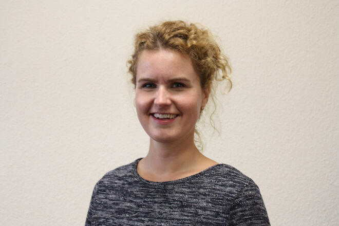 Eine Frau mit hellbraunen Locken, die hochgesteckt sind und einem graumelierten Pulli