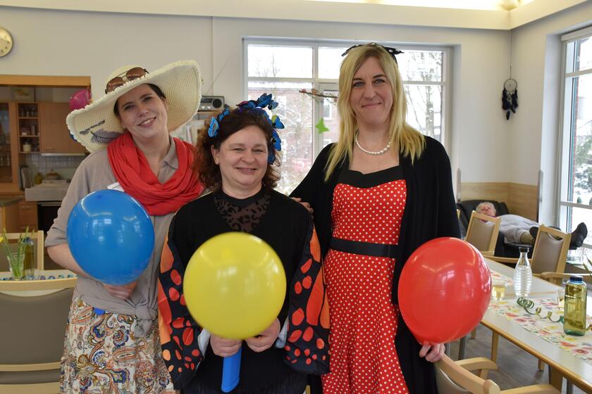 Drei Mitarbeitende sind verkleidet und halten Luftballons in Händen