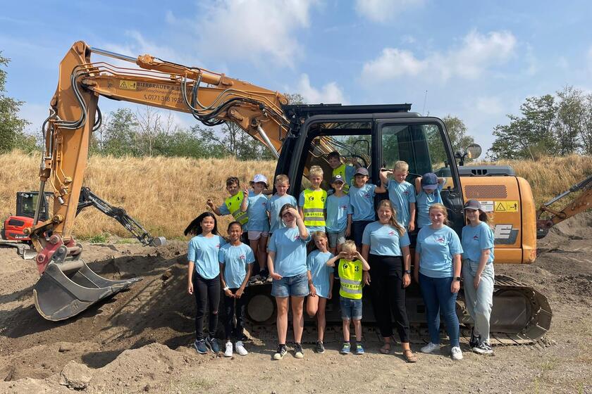 Die Kinder der Ferienbetreuung stehen vor einem Bagger