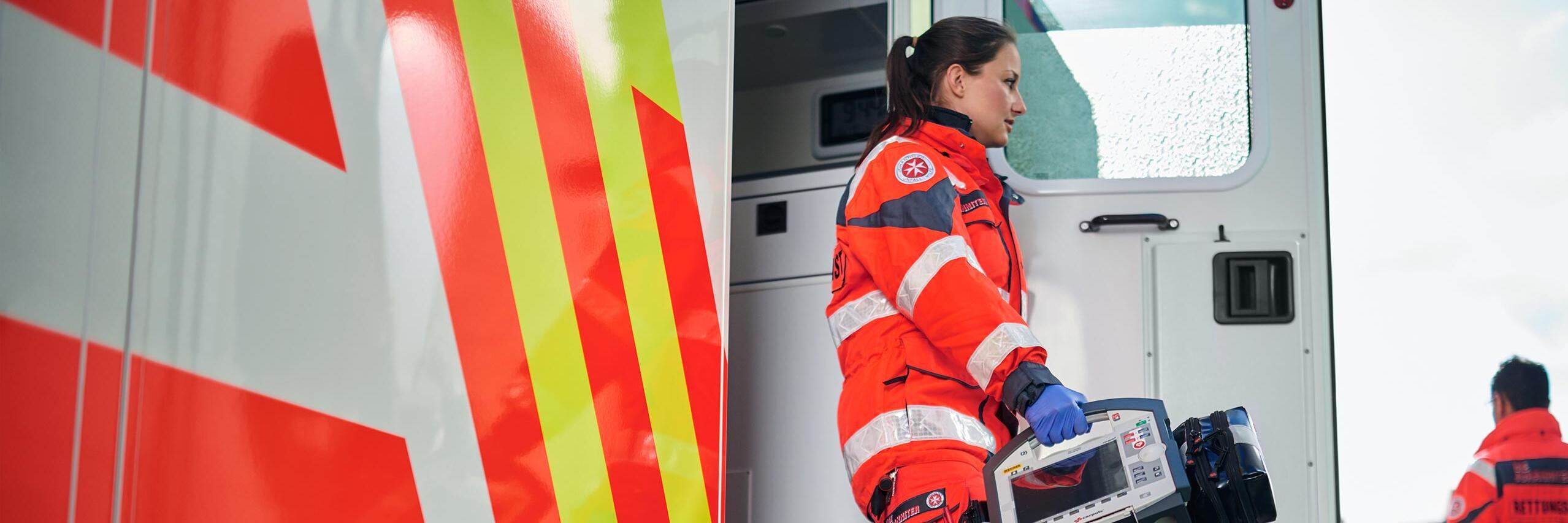 Rettungskraft der Johanniter steigt aus einem Einsatzfahrzeug und trägt medizinische Ausrüstung. Eine weitere Einsatzkraft steht daneben.
