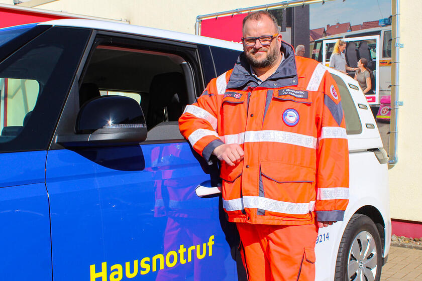 Ein Mann in Einsatzkleidung neben einem Hausnotrufeinsatzfahrzeug