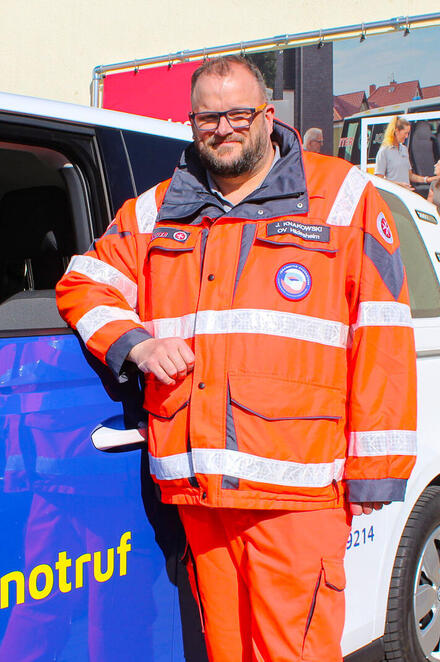 Ein Mann in Einsatzkleidung neben einem Hausnotrufeinsatzfahrzeug