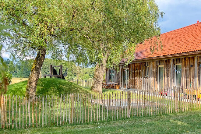 Ein grüner Garten mit Sandkasten, Rutsche und Bäumen.