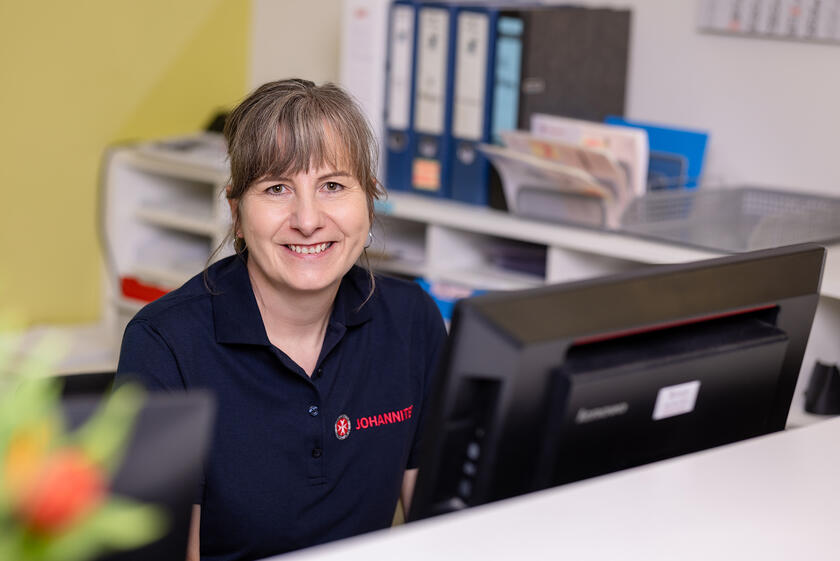 Eine Johanniterin sitzt hinter dem Rezeptionstresen in der Physiotherapie am Drägerwerk.