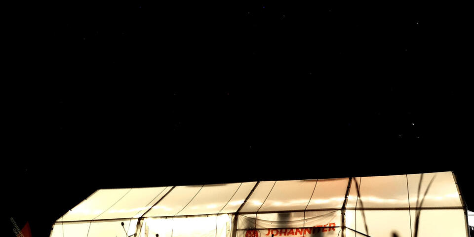 Ein Mannschaftszelt mit Aufdruck "Johanniter-Jugend" nachts, von innen beleuchtet.