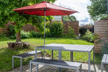 Eine Terrasse mit rotem Sonnenschirm und Gartenmöbeln im Grünen