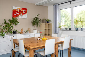 Eine Essecke mit einem Kieferntisch und weißen Stühlen. Ein Sideboards in weiß steht an der beigen Wand.