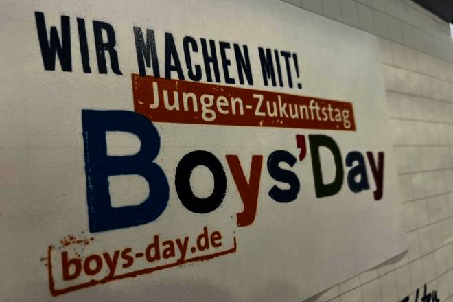 Plakat mit Schriftzug "Boys'Day" an einer weißen Wand.