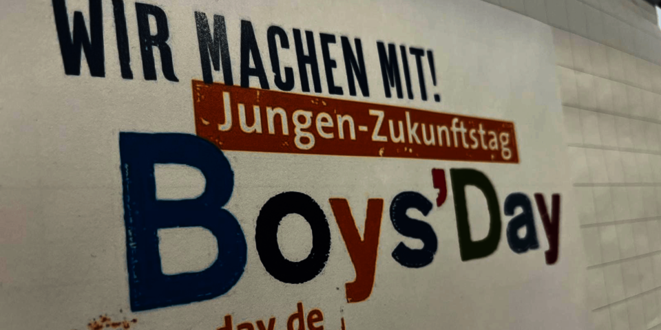 Plakat mit Schriftzug "Boys'Day" an einer weißen Wand.