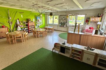 Kita Innenbereich, mit Tischen, einer grünen Wand und Teppichen.