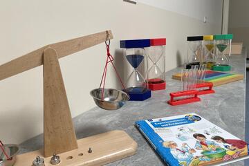 Ein Tisch mit einer Waage, bunten Sanduhren und einem Bilderbuch.