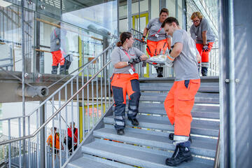 Rettungskräfte bringen eine beschwerte Trage eine Metalltreppe hinab.