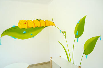 Eine gemalte Raupe mit Blättern übers Eck auf zwei Wände verteilt in grün und gelb gehalten