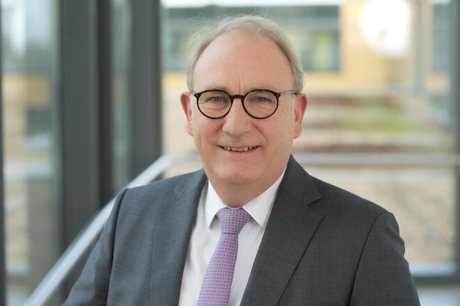 Portraitaufnahme Herr mit Brille im dunklen Anzug mit violetter Krawatte und weißem Hemd.