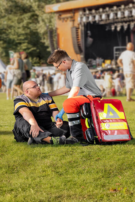 Ein Ehrenamtlicher im Sanitätsdienst betreut einem Mann auf einer Wiese