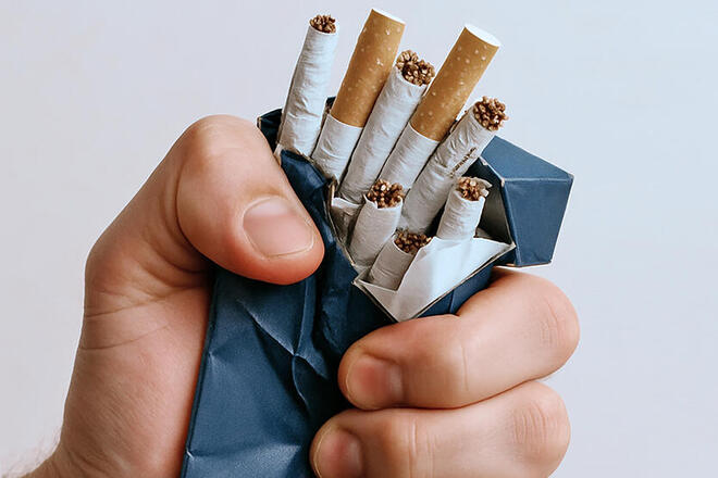 Eine Hand zerdrückt eine blaue Zigarettenschachtl