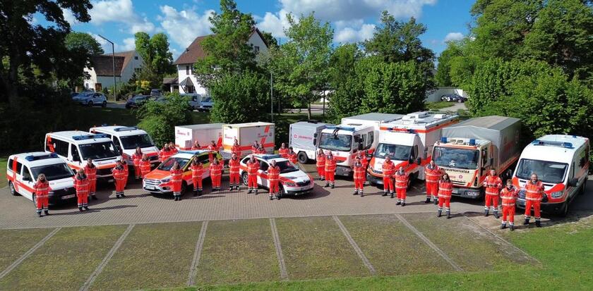 Auf dem Bild sind viele Johanniter in Einsatzkleidung zusammen mit ihren Fahrzeugen vor Bäumen zu sehen.