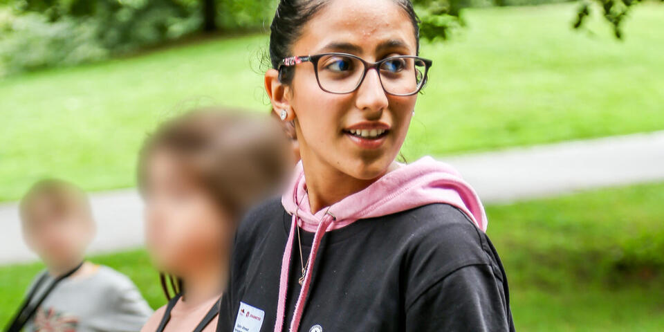 Ferienbetreuung im Freien: Betreuerin führt Kinder Hand in Hand über den Weg.