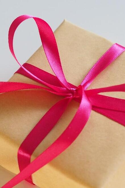Ein in braunes Papier eingepacktes Geschenk ist mit einer pinkfarbenen Schleife verziert.