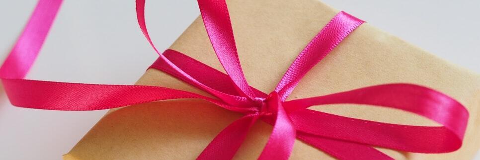 Ein in braunes Papier eingepacktes Geschenk ist mit einer pinkfarbenen Schleife verziert.