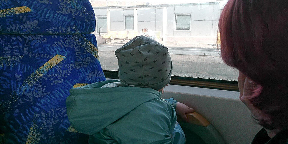 Eine Frau mit einem Kleinkind in einem Linienbus. Das Kind schaut aus dem Fenster.