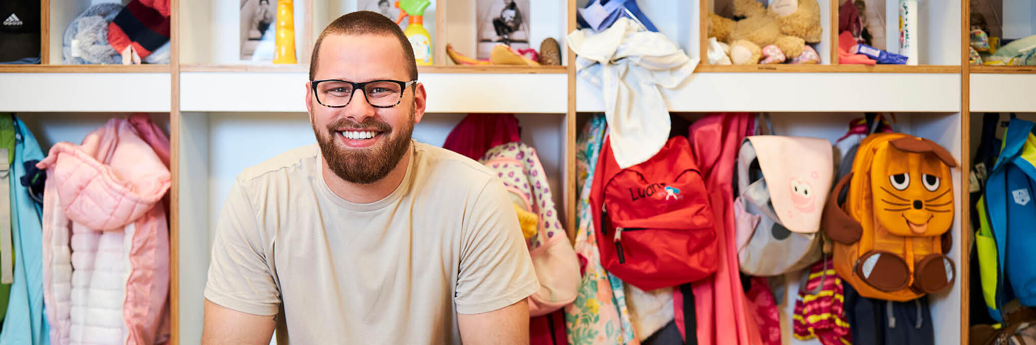 Ein Erzieher sitzt vor der Garderobe im Kindergarten.