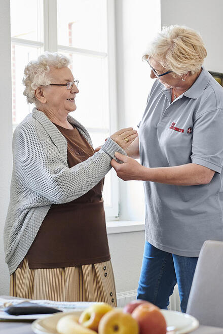 Eine Pflegerin hilft einer Frau dabei, die Ärmel ihres Oberteils hochzukrempeln.