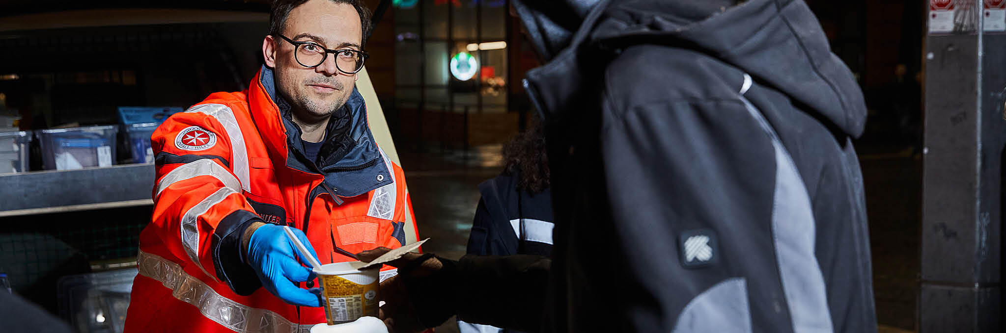 Ein Helfer des Kältebus steht am Einsatzwagen und gibt einem Obdachlosen Essen aus