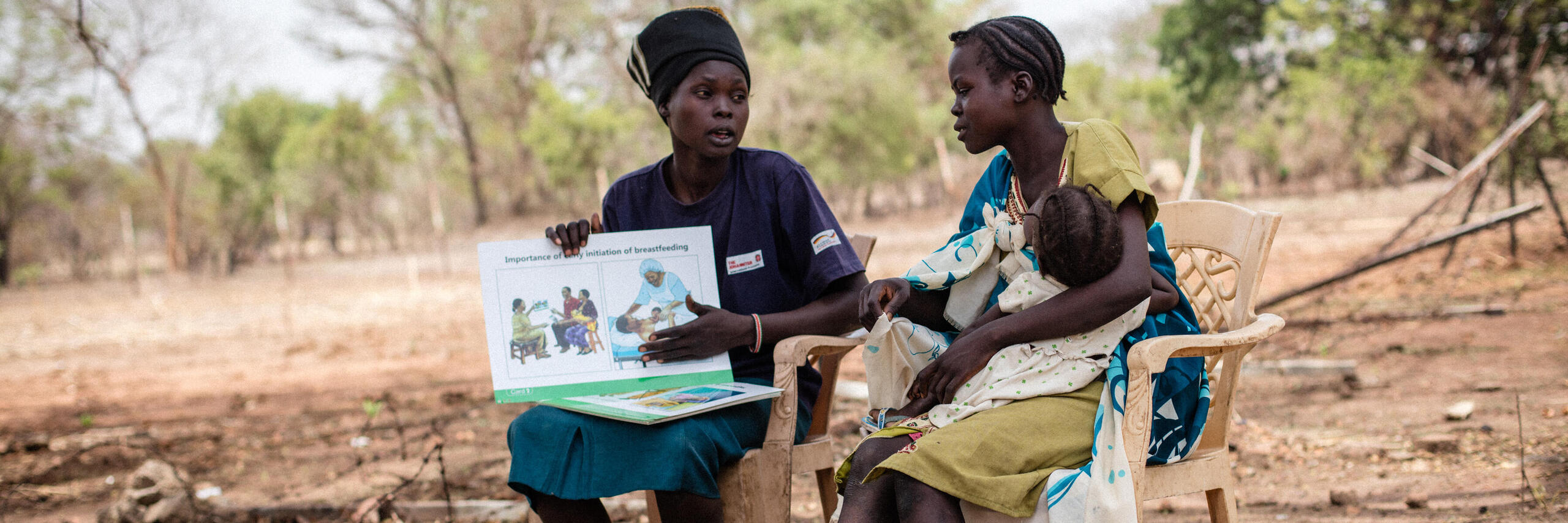 Eine Mutter erklärt einer anderen Mutter mit Säugling Vorteile des Stillens auf einem Acker. 