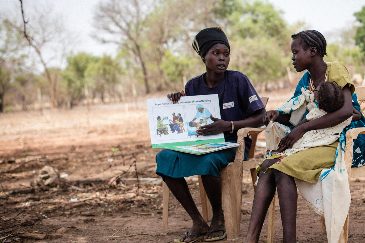 Eine Mutter erklärt einer anderen Mutter mit Säugling Vorteile des Stillens auf einem Acker. 