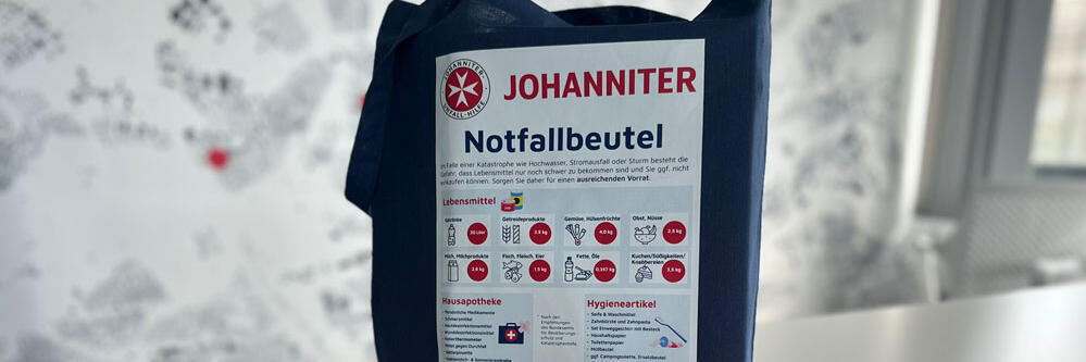 Ein blauer Bauwollbeutel mit der Überschrift "Notfallbeutel" und einer grafischen Auflistung von Bevorratungsempfehlungen.