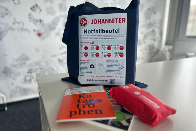 Ein blauer Bauwollbeutel mit der Überschrift "Notfallbeutel" und einer grafischen Auflistung von Bevorratungsempfehlungen.