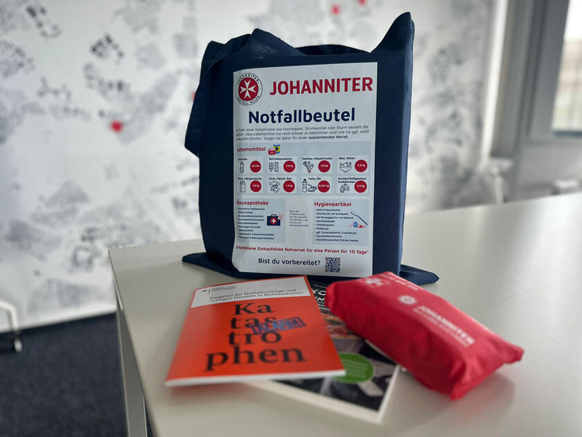 Ein blauer Bauwollbeutel mit der Überschrift "Notfallbeutel" und einer grafischen Auflistung von Bevorratungsempfehlungen.