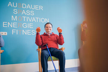 Mann im roten Pullover mit Hanteln im Fitnessraum