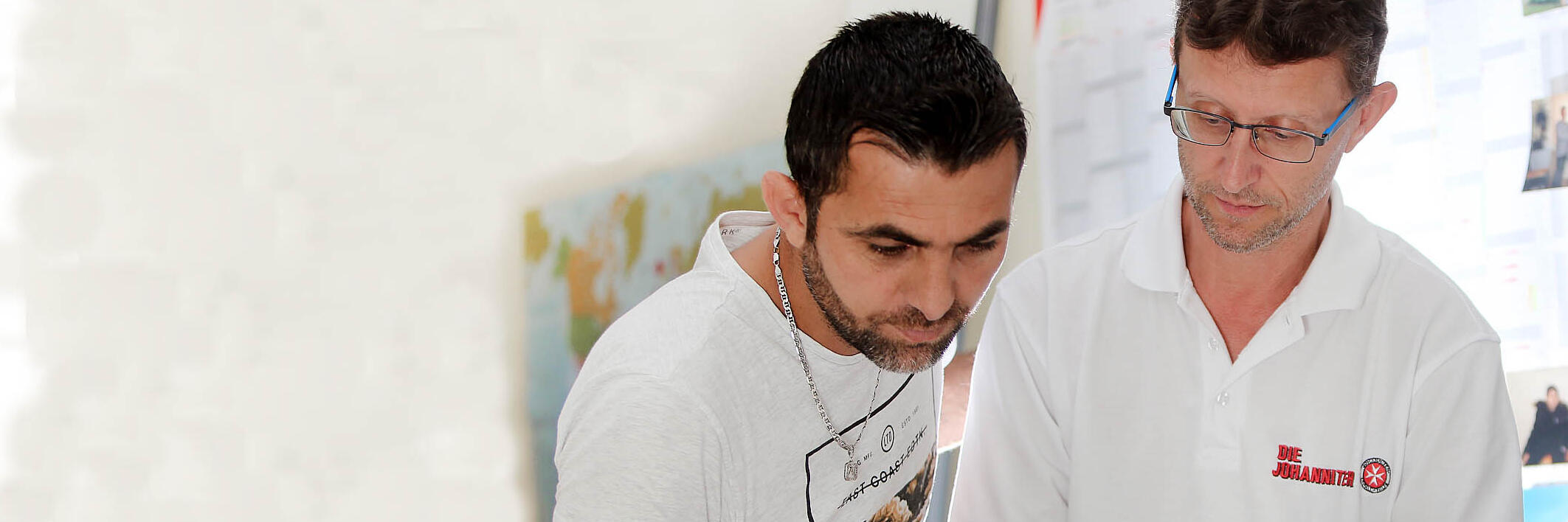 ein Mitarbeiter der Johanniter liest mit einem Bewohner einer Flüchtlingsunterkunft in einem Dokument