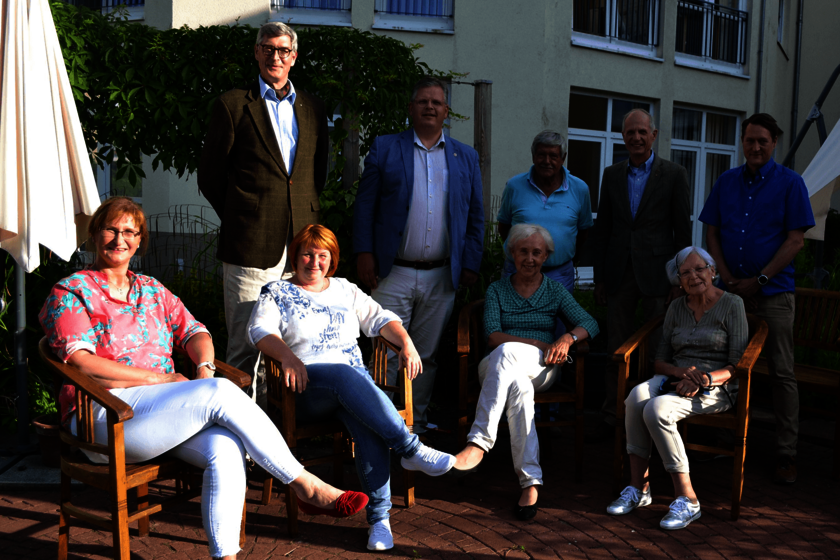 Gruppenbild mit vier Frauen, die auf einer Terrasse sitzen; dahinter stehen fünf Männer.