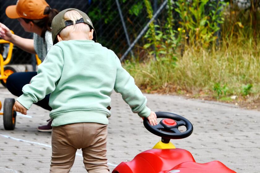 Ein kleiner Junge zeiht ein rotes Bobycar außen auf dem Pflaster mit sich mit. 