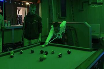 Zwei Jungen spielen Billiard am Billiardtisch, der Raum ist in grünes Licht getaucht.