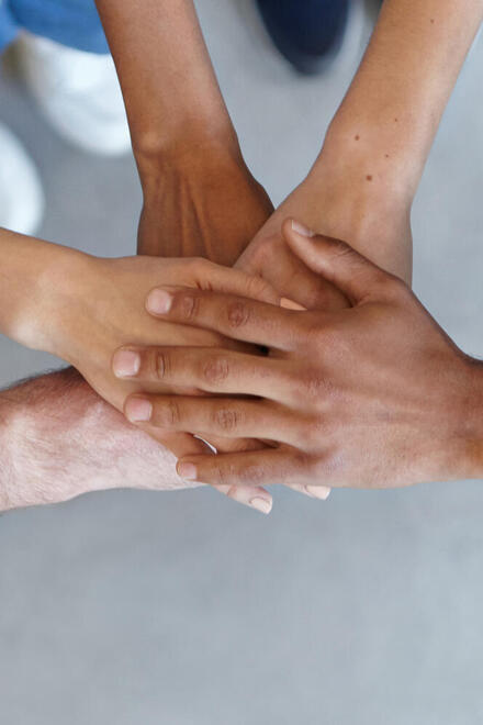 Mehrere Menschen legen ihre Hände übereinander und zeigen damit Teamgeist und Zusammenhalt.