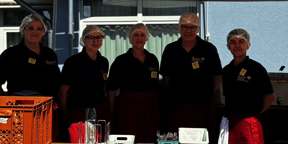 Fünf Personen im Service-Outfit stehen lächelnd hinter einem Essensstand.