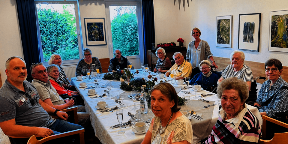 14 Personen um einen großen Tisch, alle blicken zur Kamera