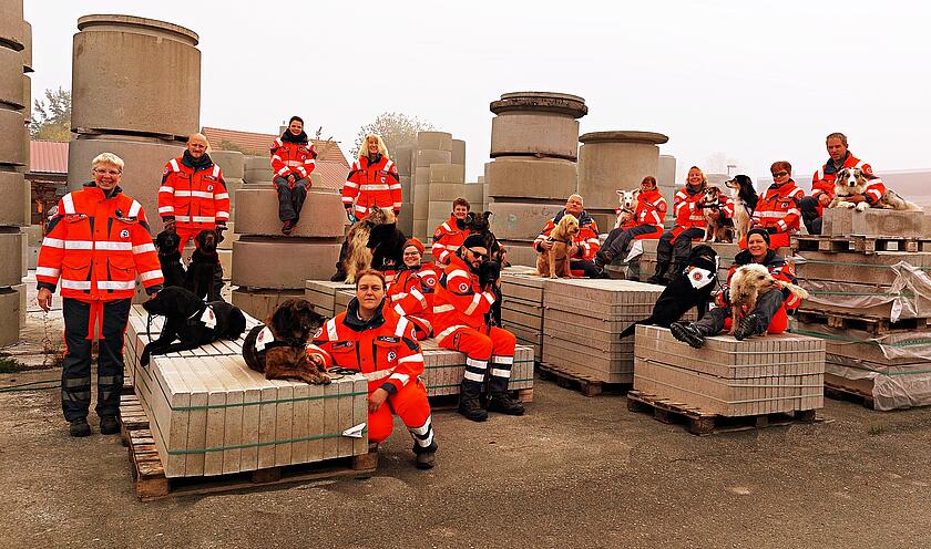 Das Bild zeigt die Mitglieder der Rettungshundestaffel in Einsatzkleidung zusammen mit ihren Hunden zwischen Betonteilen einer Baufirma.