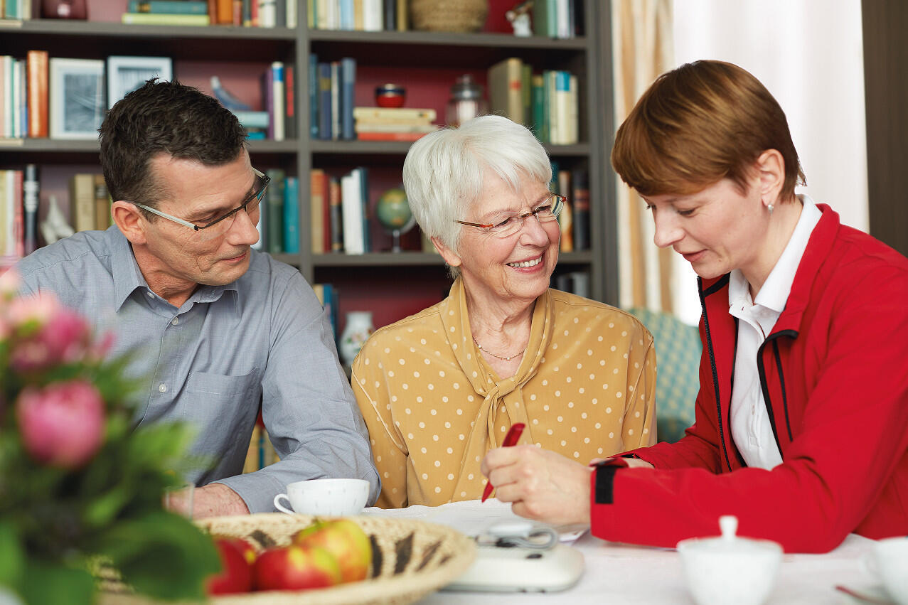 Eine Mitarbeiterin der Johanniter-Unfall-Hilfe berät einen Mann und eine Frau zum Hausnotruf.
